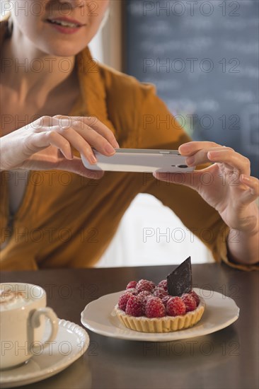 Caucasian woman taking cell phone photograph of dessert in cafe