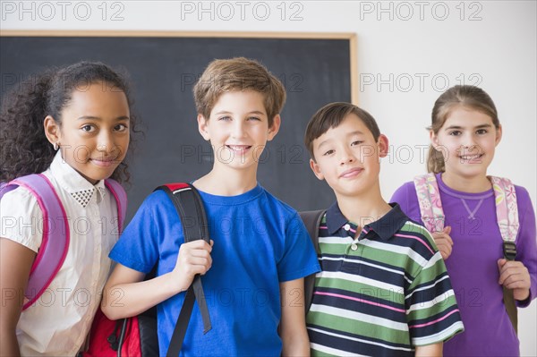 Smiling students wearing backpacks in front of chalkboard