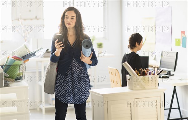 Businesswoman carrying yoga mat and cell phone in office