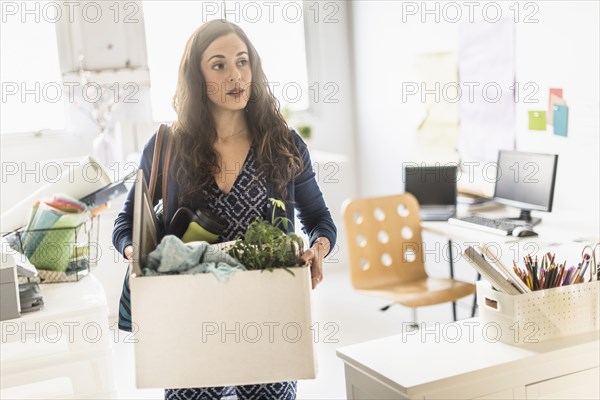 Hispanic businesswoman carrying cardboard box in office