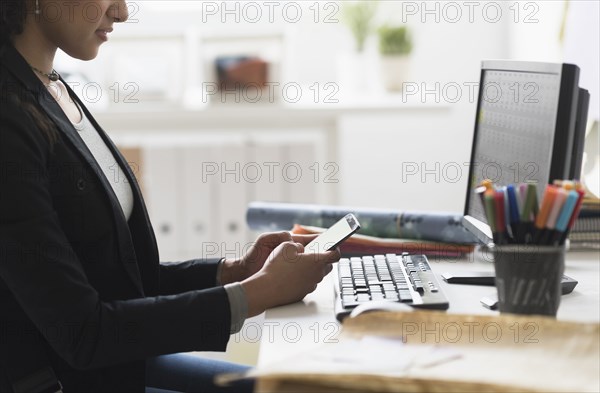 Mixed race businesswoman using cell phone at desk