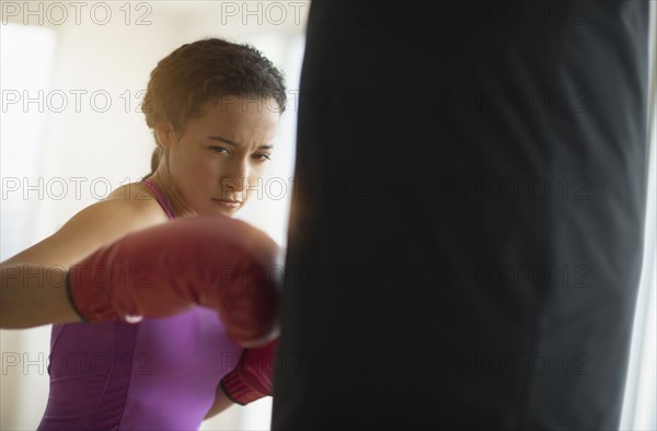 Mixed race woman hitting punching bag in gym