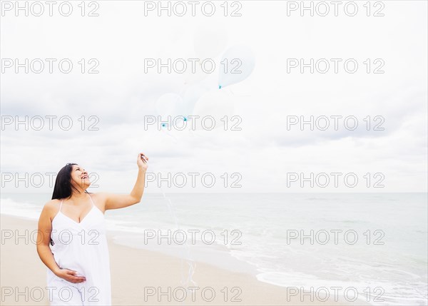 Pregnant mixed race woman holding balloons on beach