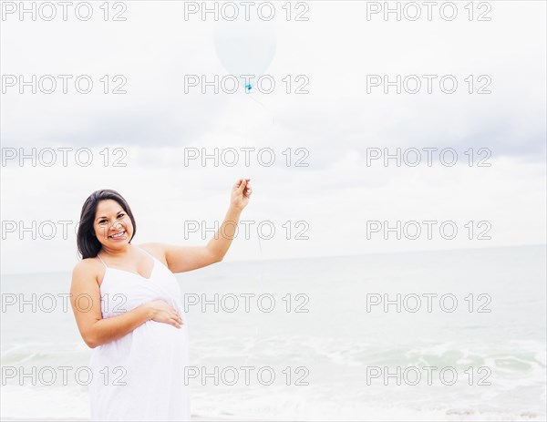 Pregnant mixed race woman holding balloon on beach