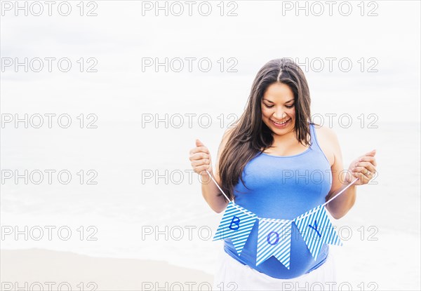 Pregnant mixed race woman holding boy banner on beach
