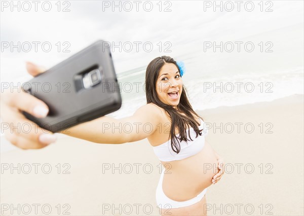 Pregnant mixed race woman taking cell phone photograph on beach