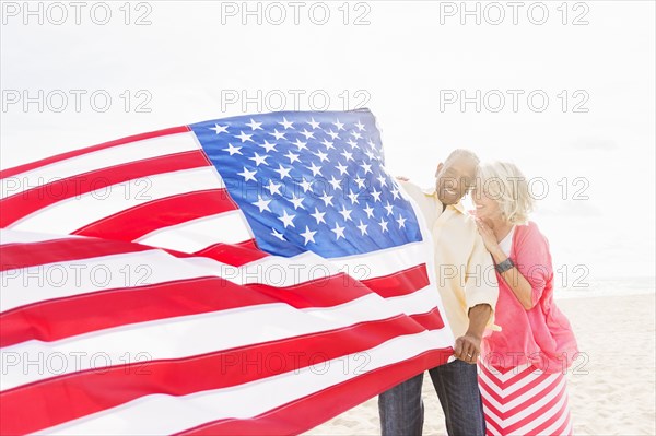 Older couple holding American flag on beach