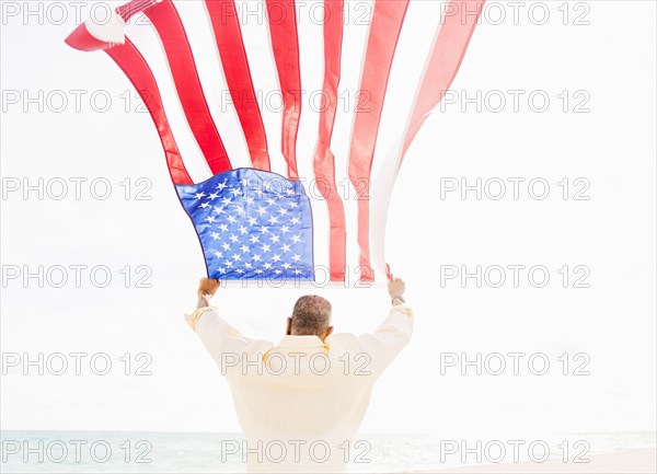 Older mixed race man holding American flag on beach