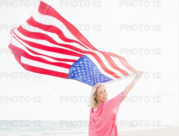 Older Caucasian woman holding American flag on beach