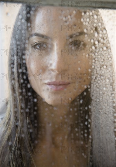 Caucasian woman peering through wet window