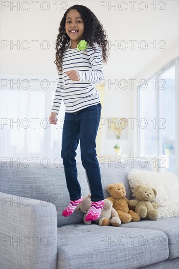 Mixed race girl jumping on sofa
