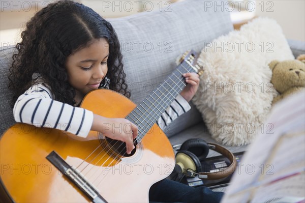 Mixed race girl practicing guitar on sofa