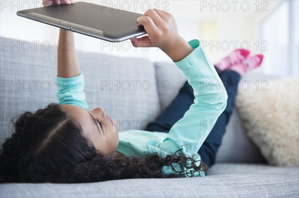 Mixed race girl using digital tablet on sofa