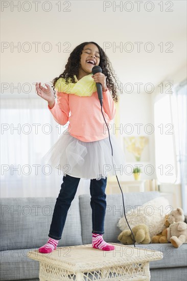 Mixed race girl singing on living room table