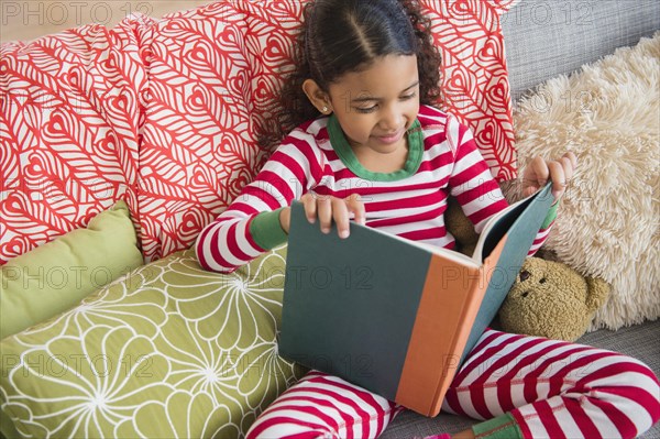 Mixed race girl reading book on sofa