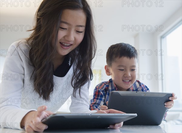 Asian brother and sister using digital tablets at table