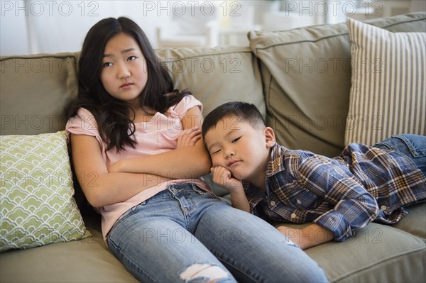 Bored Asian brother and sister relaxing on sofa