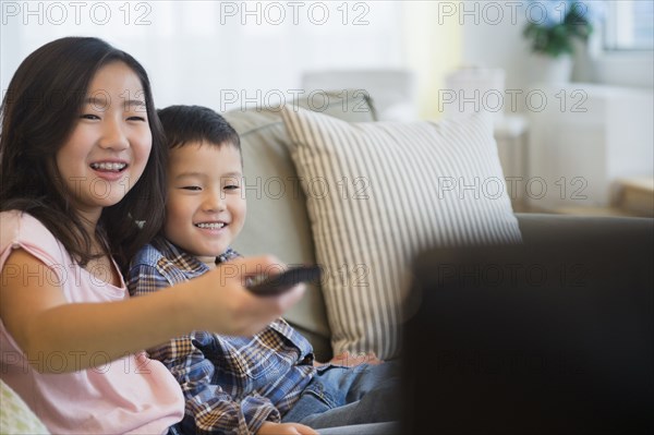 Asian brother and sister watching television on sofa