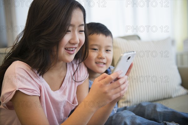 Asian brother and sister using cell phone on sofa