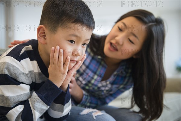 Asian sister comforting sad brother on sofa