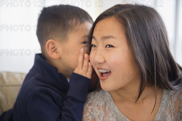 Asian boy whispering in ear of sister