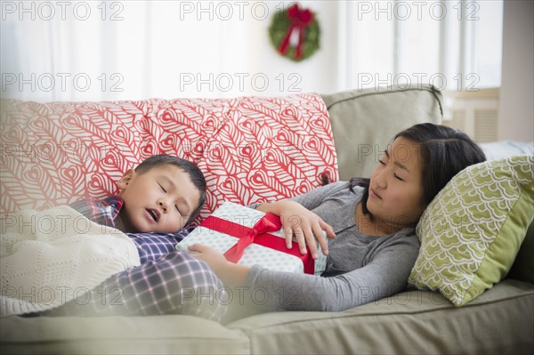 Asian brother and sister napping on sofa with Christmas gift