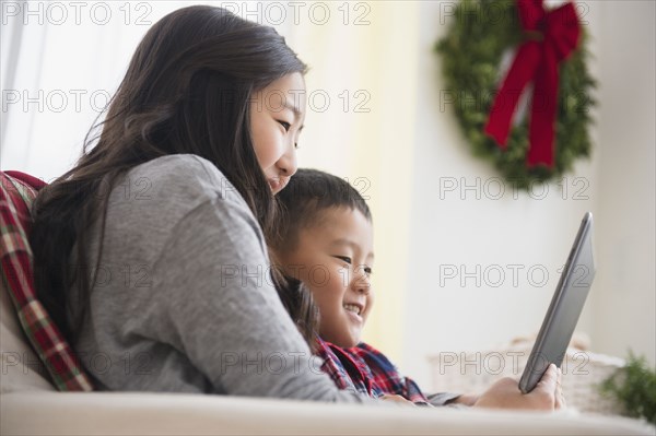 Asian brother and sister using laptop on sofa