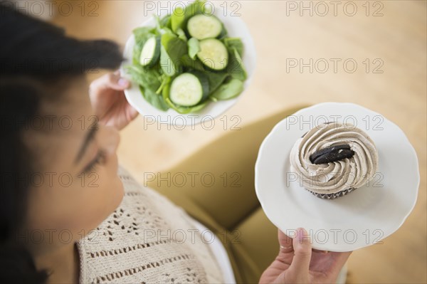 Pacific Islander woman choosing between cupcake and salad