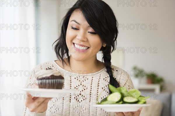 Pacific Islander woman choosing between cupcake and salad