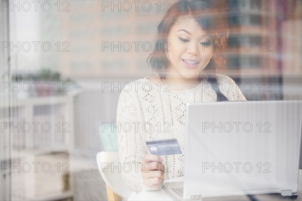 Pacific Islander woman shopping online on laptop behind window