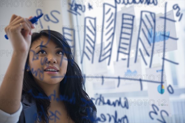 Pacific Islander businesswoman drawing chart on glass in office