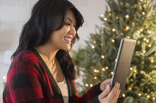 Pacific Islander woman using digital tablet near Christmas tree