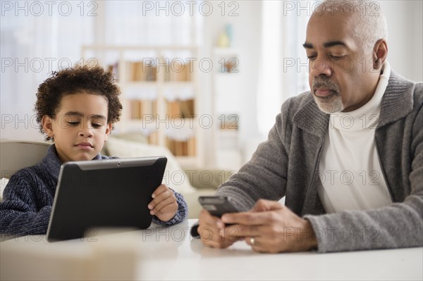 Mixed race grandfather and grandson using cell phone and digital tablet