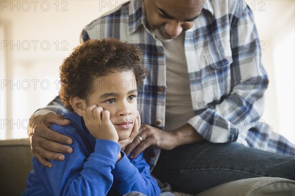 Mixed race grandfather comforting grandson on sofa