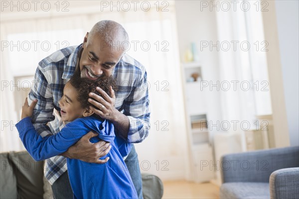 Mixed race grandfather and grandson hugging in living room