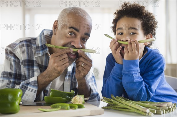 Mixed race grandfather and grandson making mustaches with asparagus