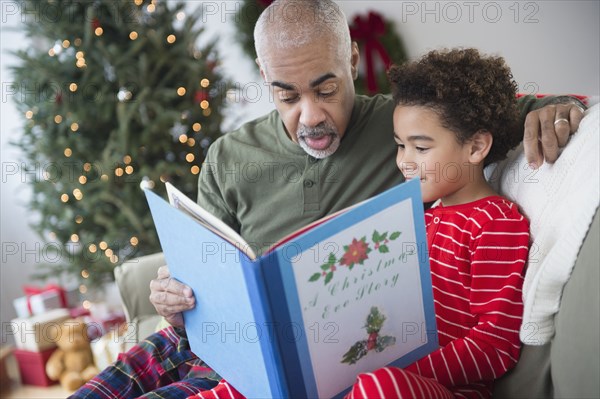 Mixed race grandfather reading to grandson at Christmas