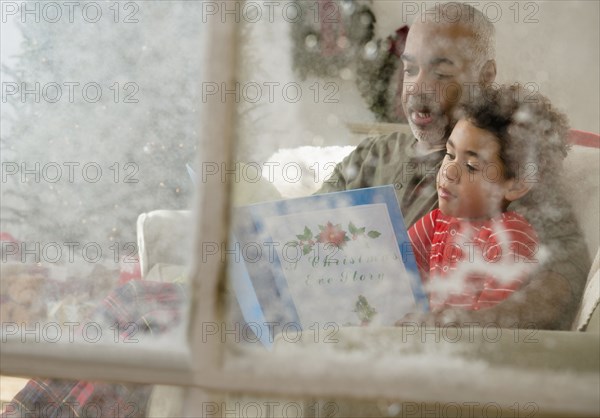 Mixed race grandfather reading to grandson behind window at Christmas