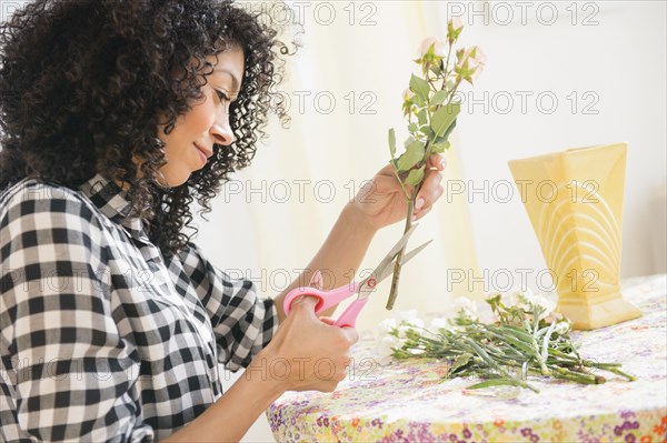 Mixed race woman cutting flower stems at table