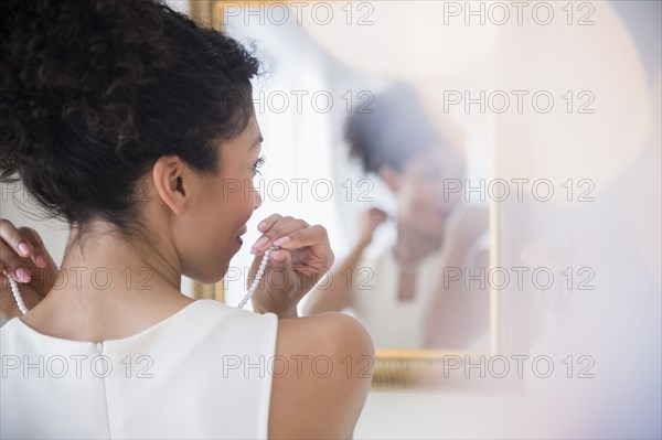Mixed race woman fastening pearl necklace in mirror