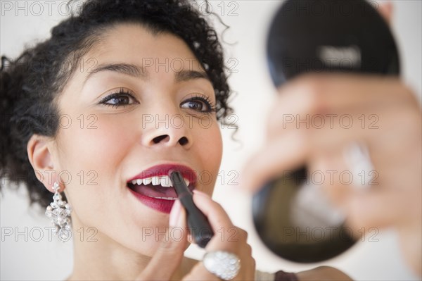 Mixed race woman applying lipstick in compact mirror