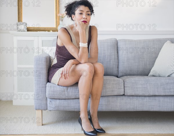 Mixed race woman in cocktail dress sitting on sofa