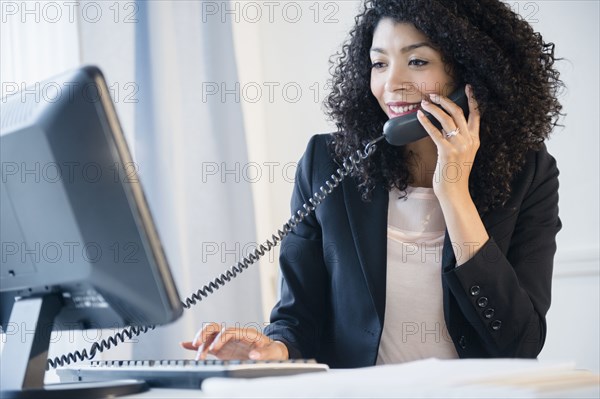 Mixed race businesswoman using telephone and computer in office