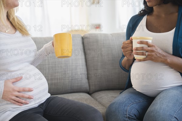 Pregnant women drinking coffee and talking on sofa