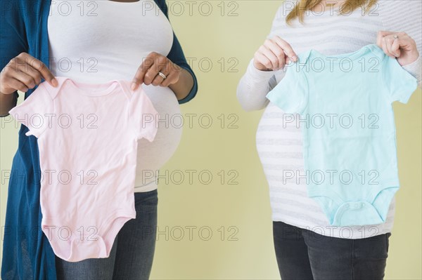 Pregnant women holding boy and girl baby clothes