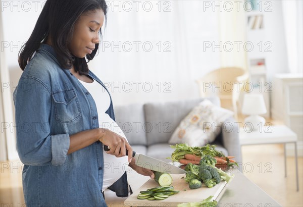 Black pregnant woman chopping vegetables in kitchen