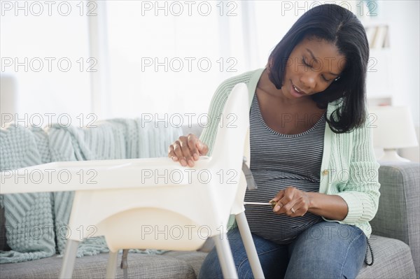 Black pregnant woman assembling high chair in living room