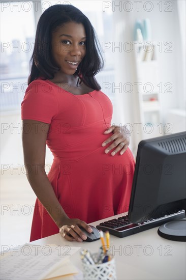 Black pregnant businesswoman working at computer in office