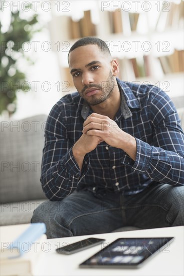 Hispanic man with cell phone and digital tablet in living room