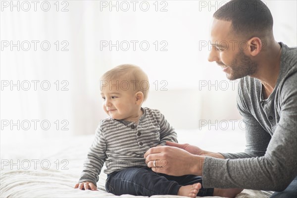 Father playing with baby son on bed